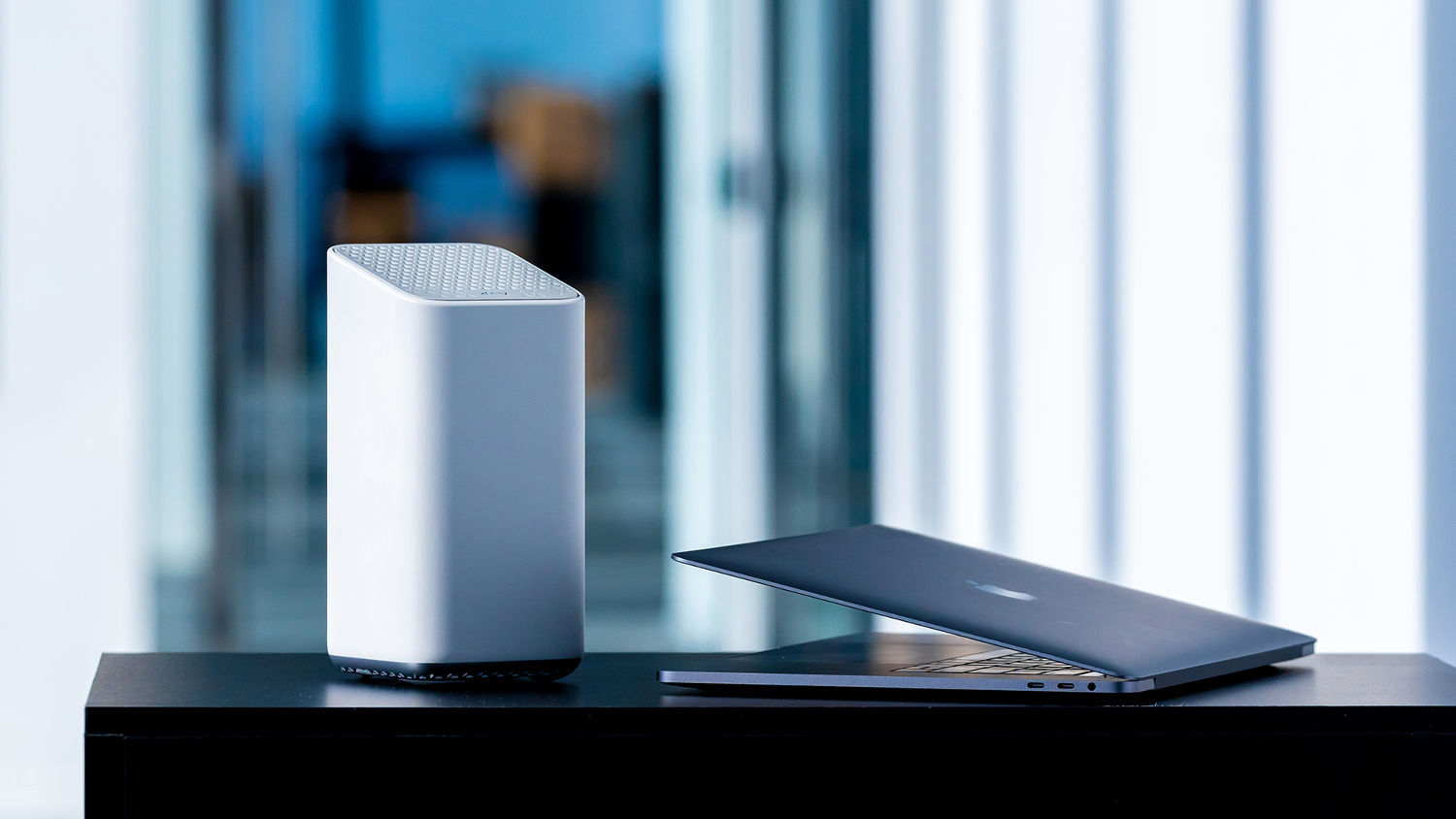A laptop rests next to a smart speaker.