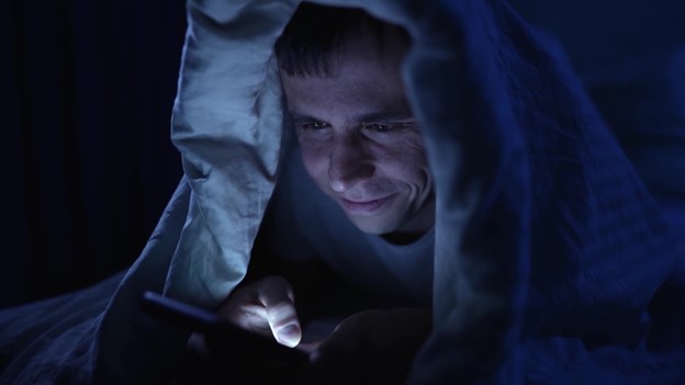 A man under a blanket with a flashlight.